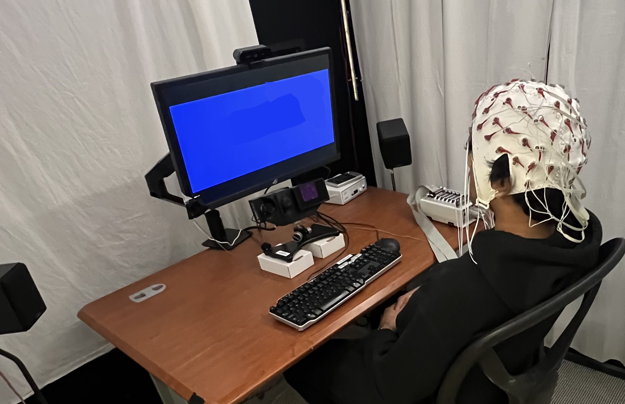 Picture of a participant sitting in the experiment booth with electrodes placed at the respective modalities' locations.